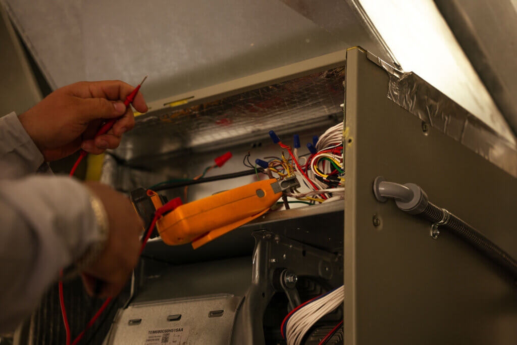 An HVAC contractor is inspecting the wires in an HVAC system while performing maintenance services